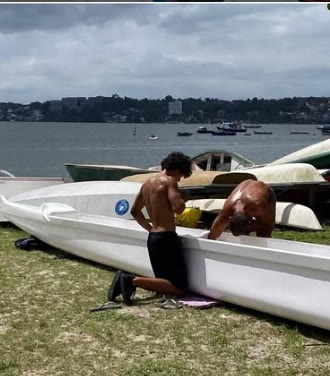 Gabriel e Rodrigo preparando a canoa Hale Hoe na grama, de frente para a baía