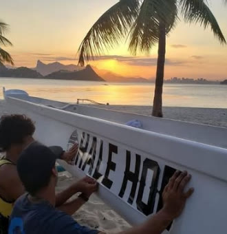 Remadores pintando o nome Hale Hoe na canoa ao pôr do sol
